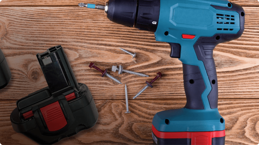 A blue cordless drill sitting on a table along with loose screws and an extra battery pack