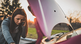 Woman talking on her mobile phone while looking down at her car engine